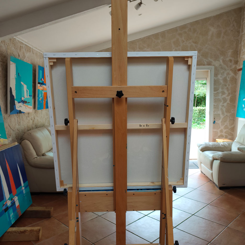 Envers d'un tableau carré posé sur un chevalet en bois dans un atelier d'artiste montrant le châssis en bois et la toile tendue.
