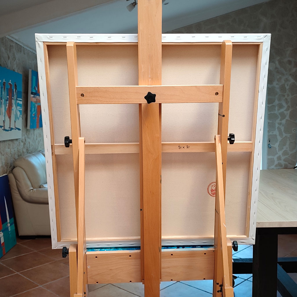 Verso d'un châssis entoilé de format 80x80 cm posé sur un chevalet d'artiste en bois dans un atelier.