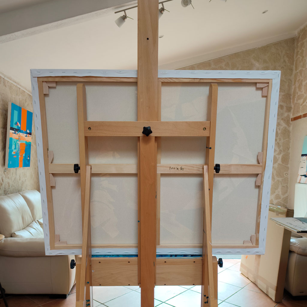 Envers de la toile 100x80 cm posée sur un chevalet en bois dans l'atelier de l'artiste, montrant le châssis en bois et les clés de tension