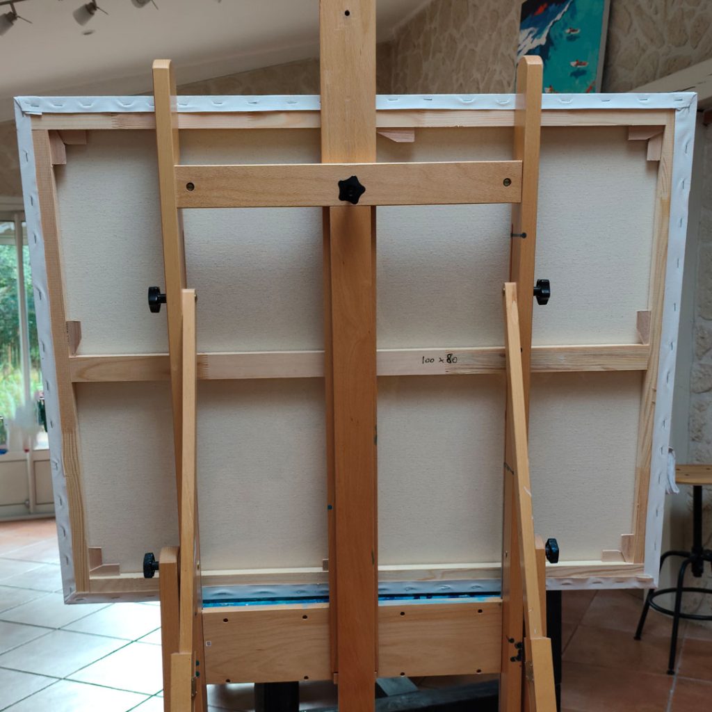 Envers de la toile d'artiste Un dimanche au lagon posée sur un chevalet en bois avec l'inscription des dimensions 100x80 cm